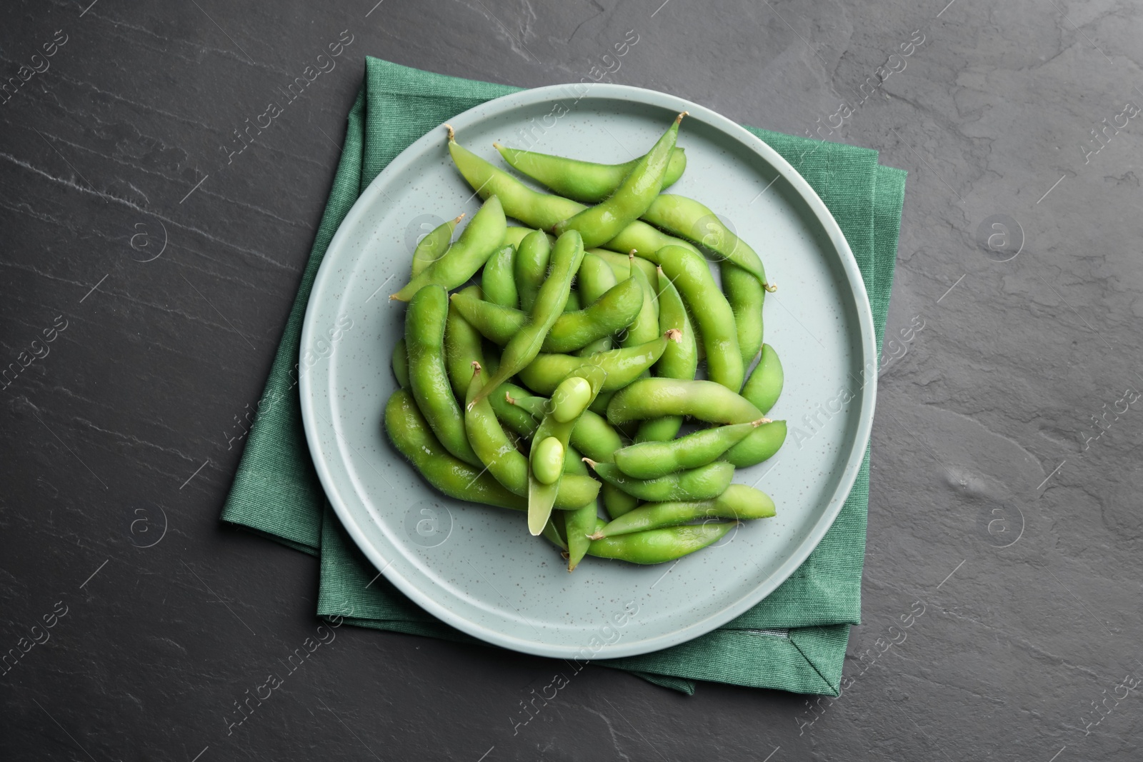 Photo of Plate of green edamame beans in pods on black table, top view