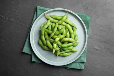 Photo of Plate of green edamame beans in pods on black table, top view