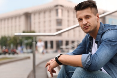 Portrait of handsome young man sitting on stairs outdoors. Space for text