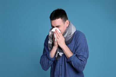 Photo of Young man blowing nose in tissue on blue background. Cold symptoms