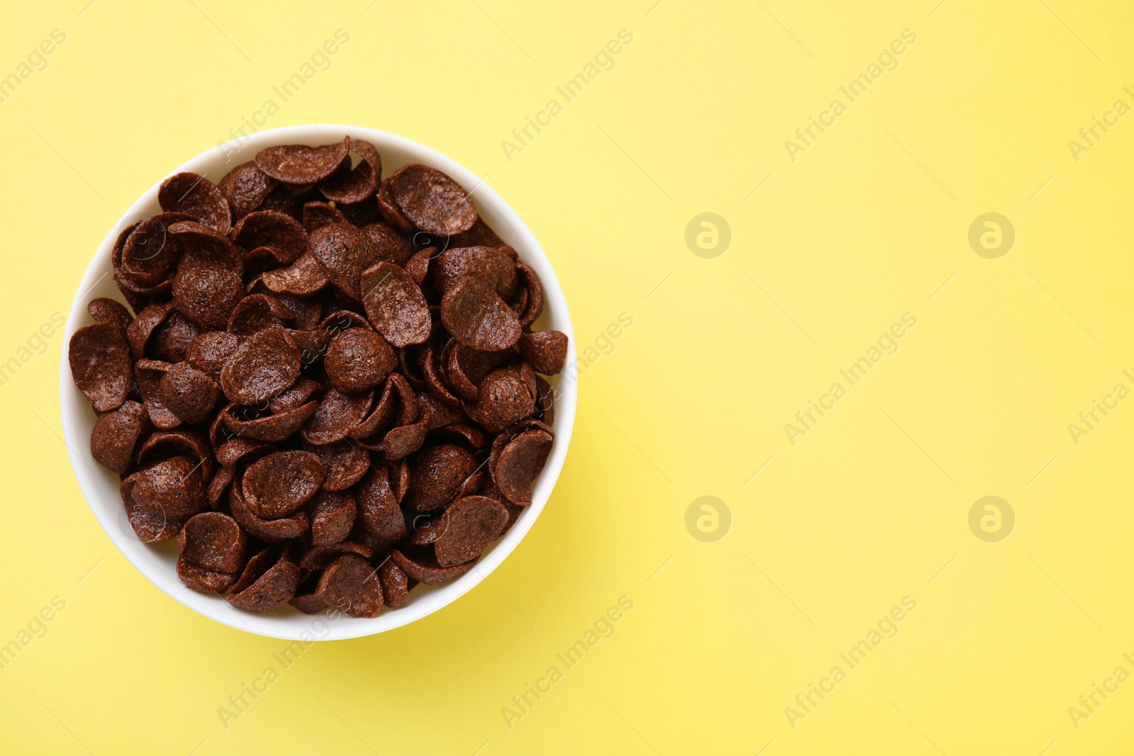 Photo of Breakfast cereal. Chocolate corn flakes in bowl on yellow table, top view. Space for text