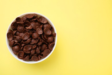 Breakfast cereal. Chocolate corn flakes in bowl on yellow table, top view. Space for text