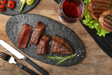 Photo of Delicious sliced beef tenderloin served on wooden table, flat lay