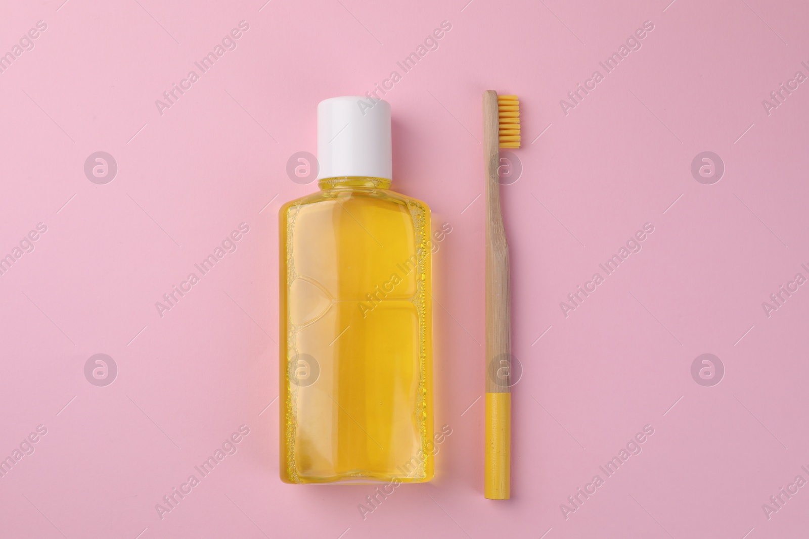 Photo of Fresh mouthwash in bottle and toothbrush on pink background, top view