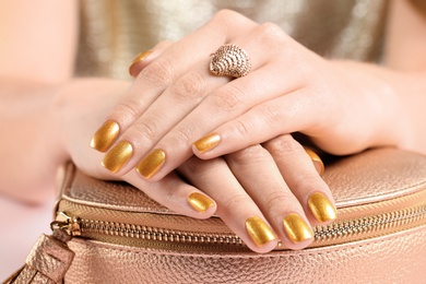 Woman holding manicured hands with golden nail polish on bag, closeup