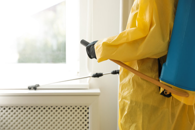 Photo of Pest control worker spraying pesticide on window sill indoors, closeup