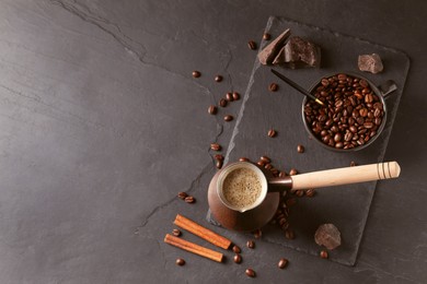 Photo of Cezve with Turkish coffee, beans and cinnamon on dark grey table, flat lay. Space for text