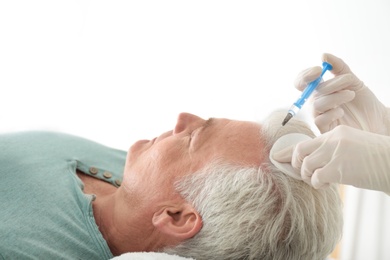 Photo of Senior man with hair loss problem receiving injection in salon