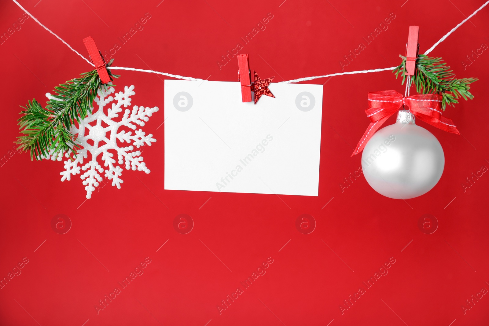 Photo of Blank Christmas card and festive decor on rope against red background, space for text