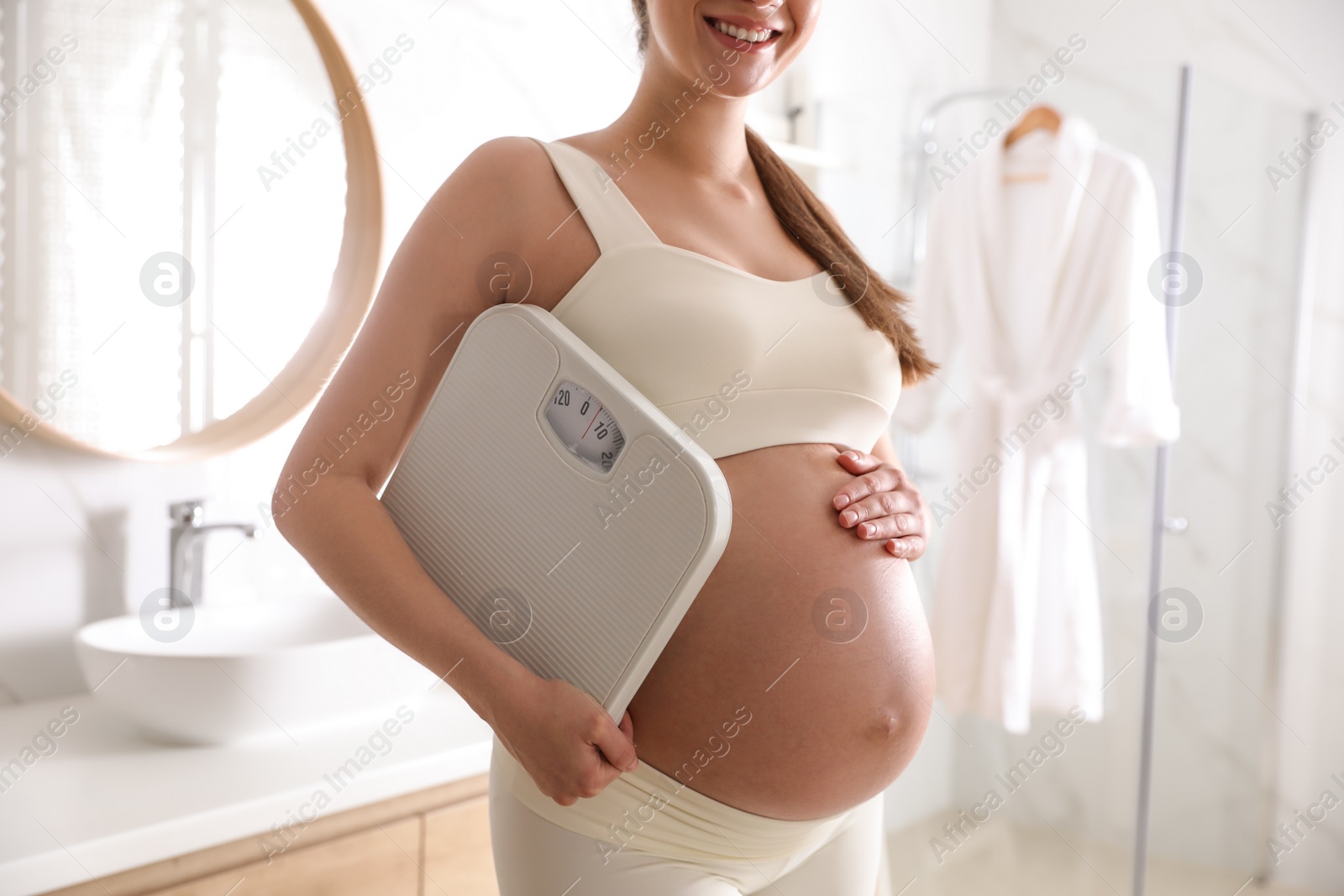 Photo of Young pregnant woman with scales in bathroom, closeup