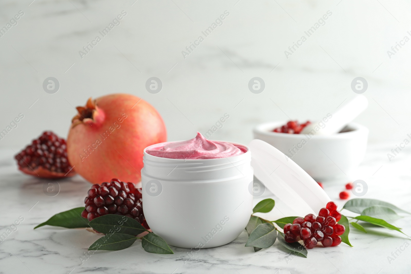 Photo of Fresh pomegranate and jar of facial mask on white marble table. Natural organic cosmetics