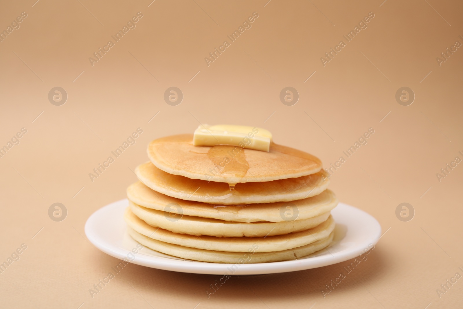 Photo of Delicious pancakes with butter and honey on beige background