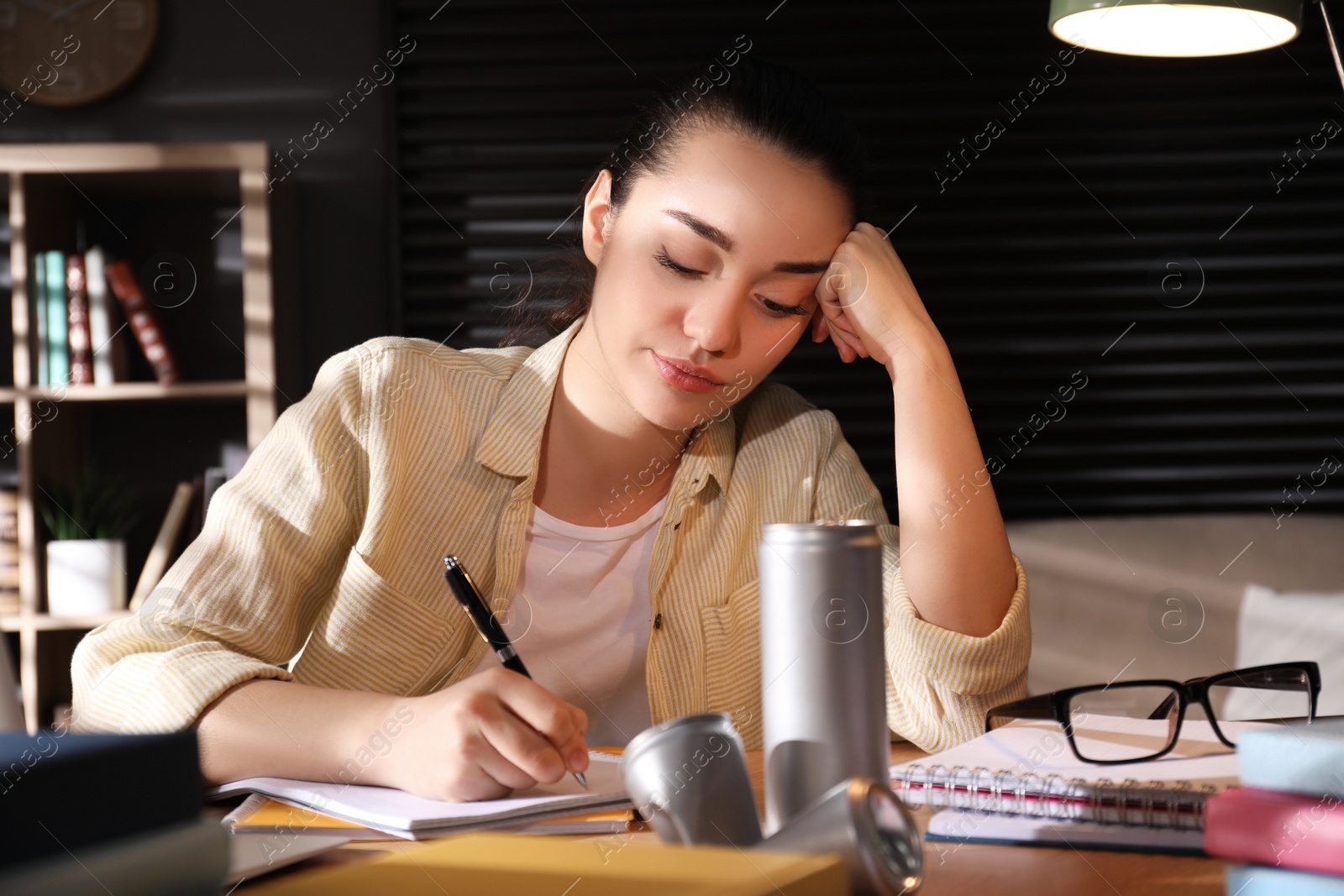 Photo of Tired young woman with energy drink studying at home