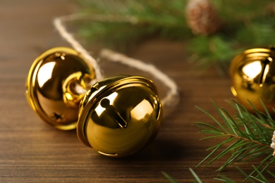 Photo of Golden sleigh bells and fir branch on wooden table, closeup