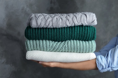 Photo of Woman holding stack of warm clothes on dark background, closeup. Autumn season