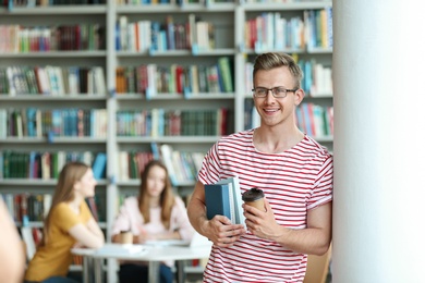 Photo of Young man with books and drink in library. Space for text
