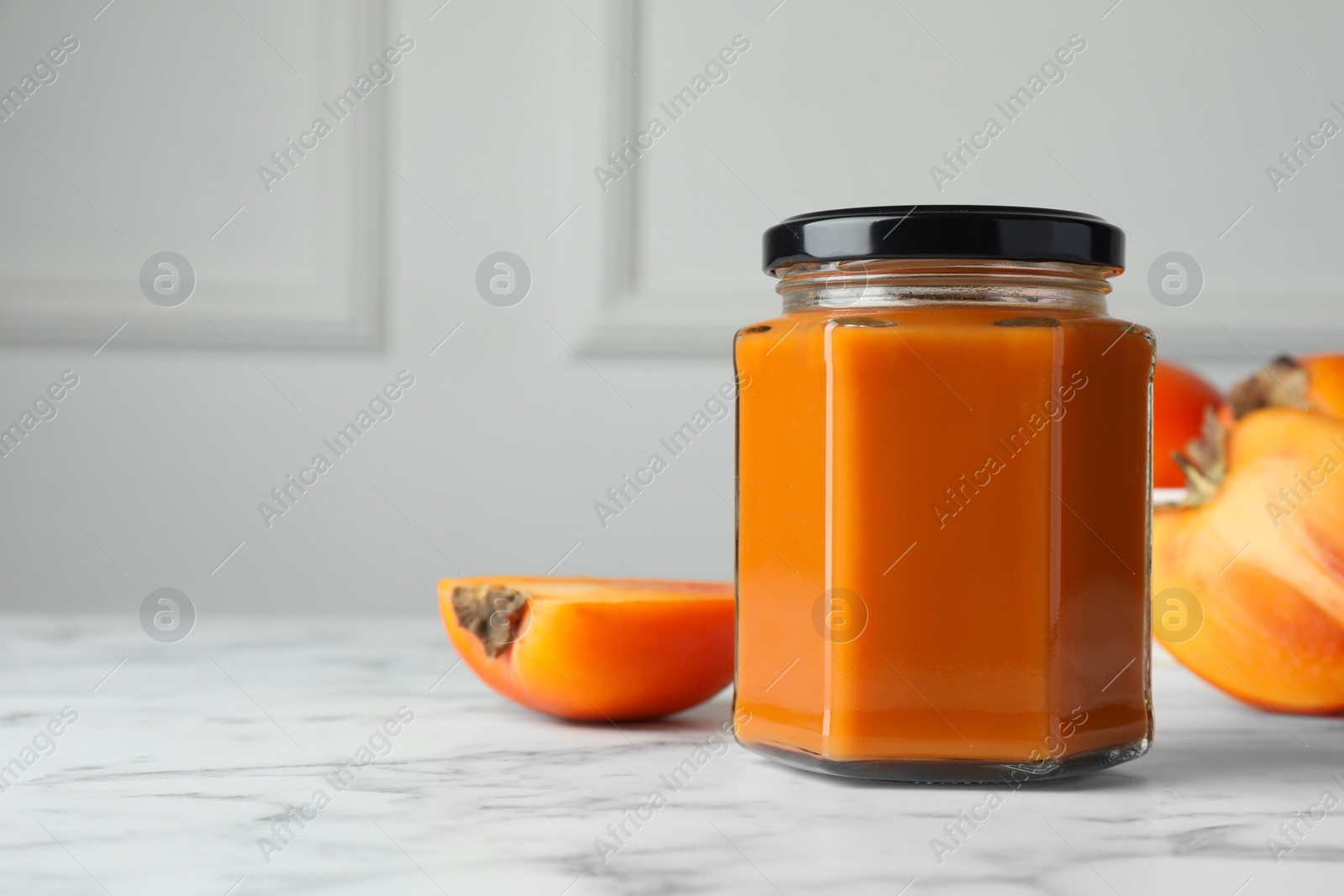 Photo of Delicious persimmon jam and fresh fruits on white marble table. Space for text