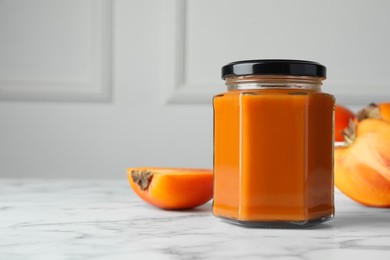 Photo of Delicious persimmon jam and fresh fruits on white marble table. Space for text