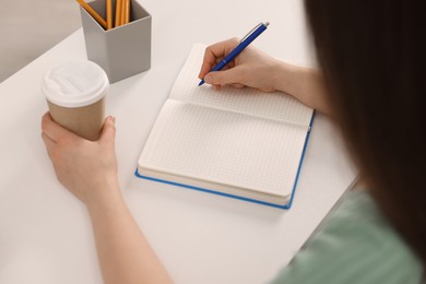 Young woman writing in notebook at white table, closeup