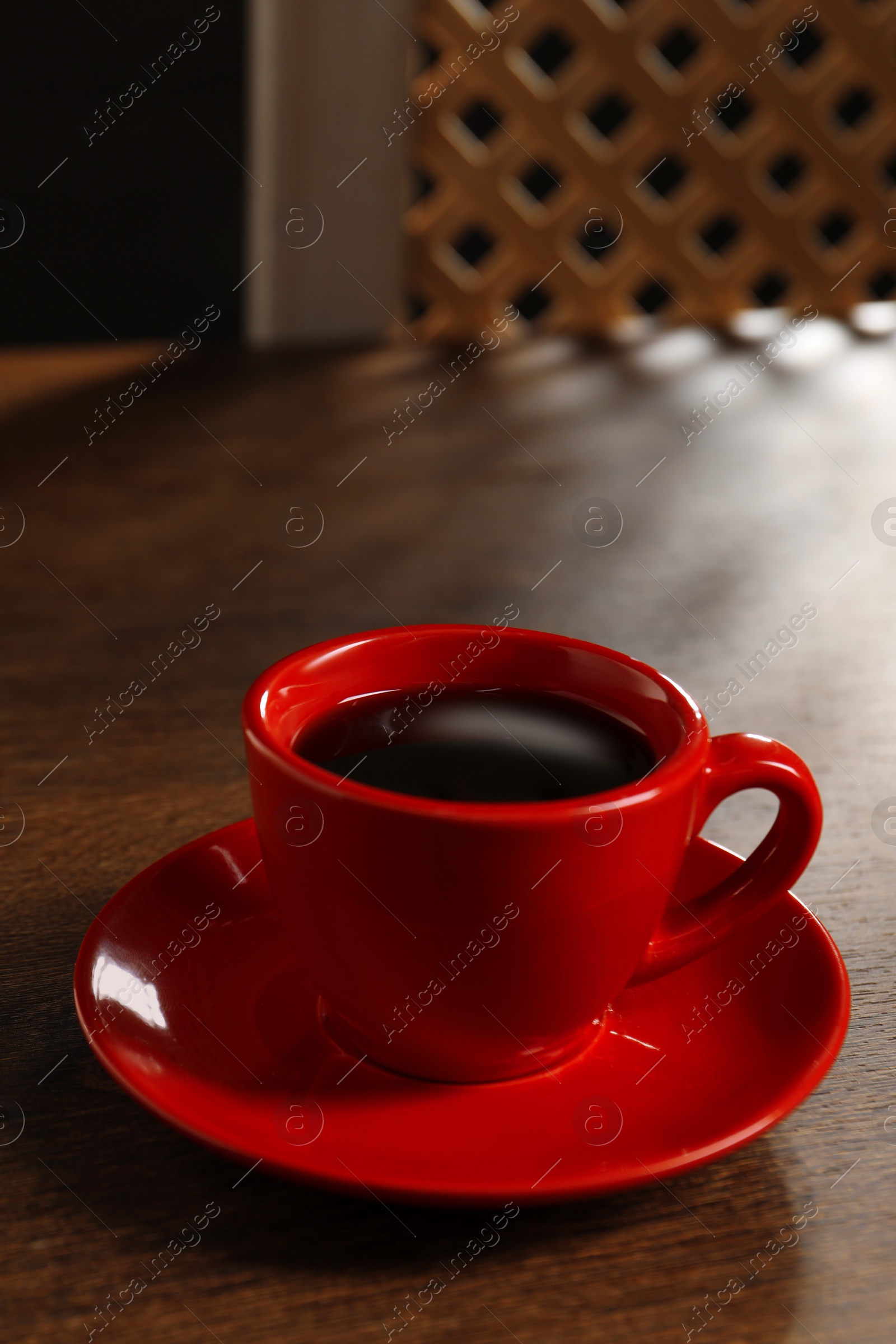 Photo of Red cup with aromatic coffee on wooden table indoors, closeup