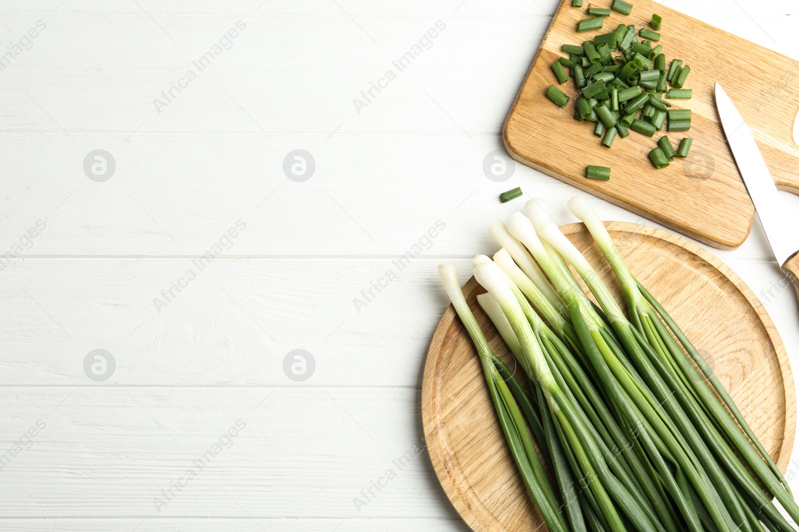 Photo of Fresh green spring onions, knife and cutting board on white wooden table, flat lay. Space for text