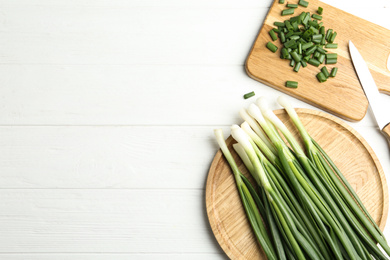 Fresh green spring onions, knife and cutting board on white wooden table, flat lay. Space for text