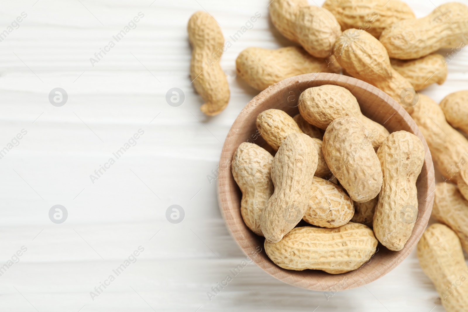 Photo of Fresh peanuts in bowl on white wooden table, top view. Space for text