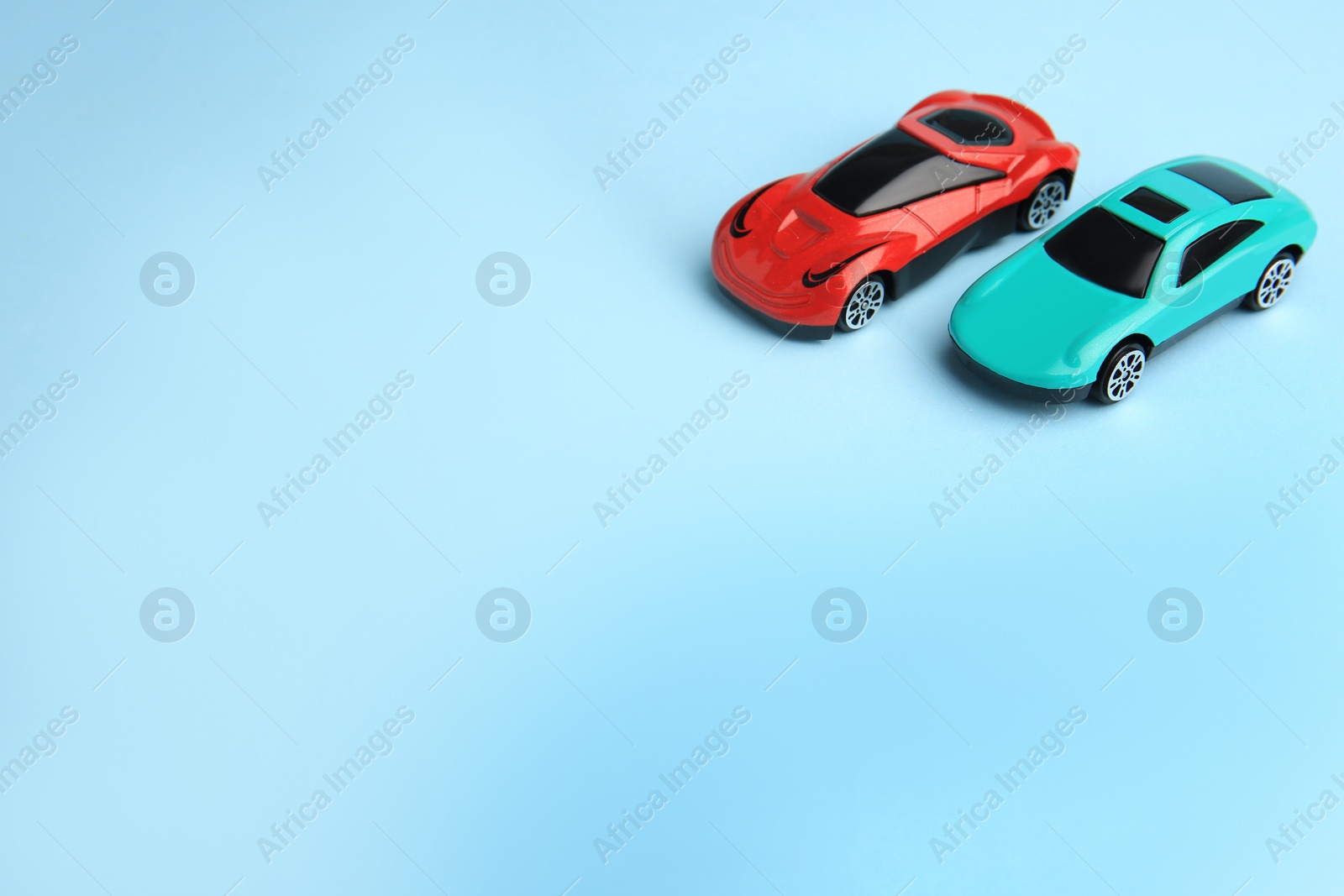 Photo of Two bright cars on light blue background, space for text. Children`s toys