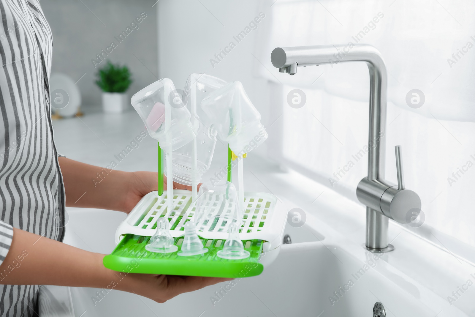 Photo of Woman holding dryer with baby bottles and nipples in kitchen, closeup