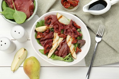 Photo of Delicious bresaola salad with sun-dried tomatoes, pear and balsamic vinegar served on white wooden table, flat lay