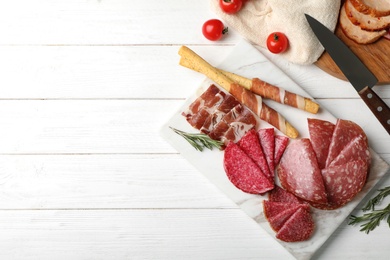 Photo of Cutting board with different sliced meat products on wooden background, flat lay. Space for text
