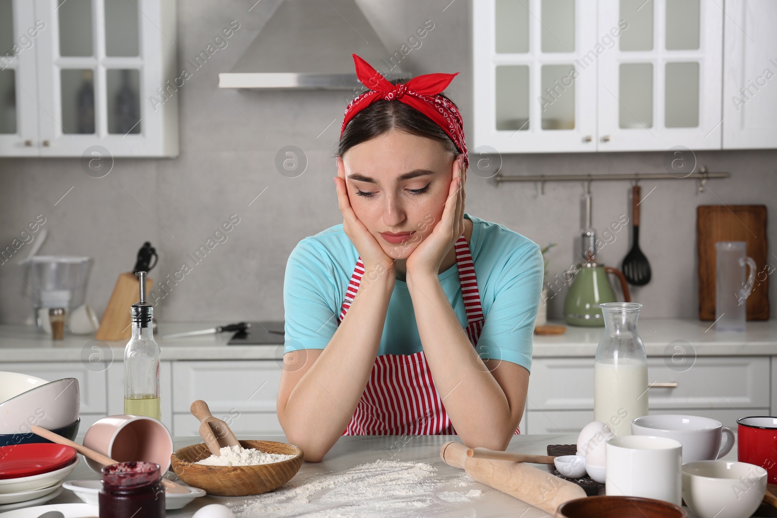 Photo of Upset housewife at messy countertop in kitchen. Many dirty dishware, food leftovers and utensils on table