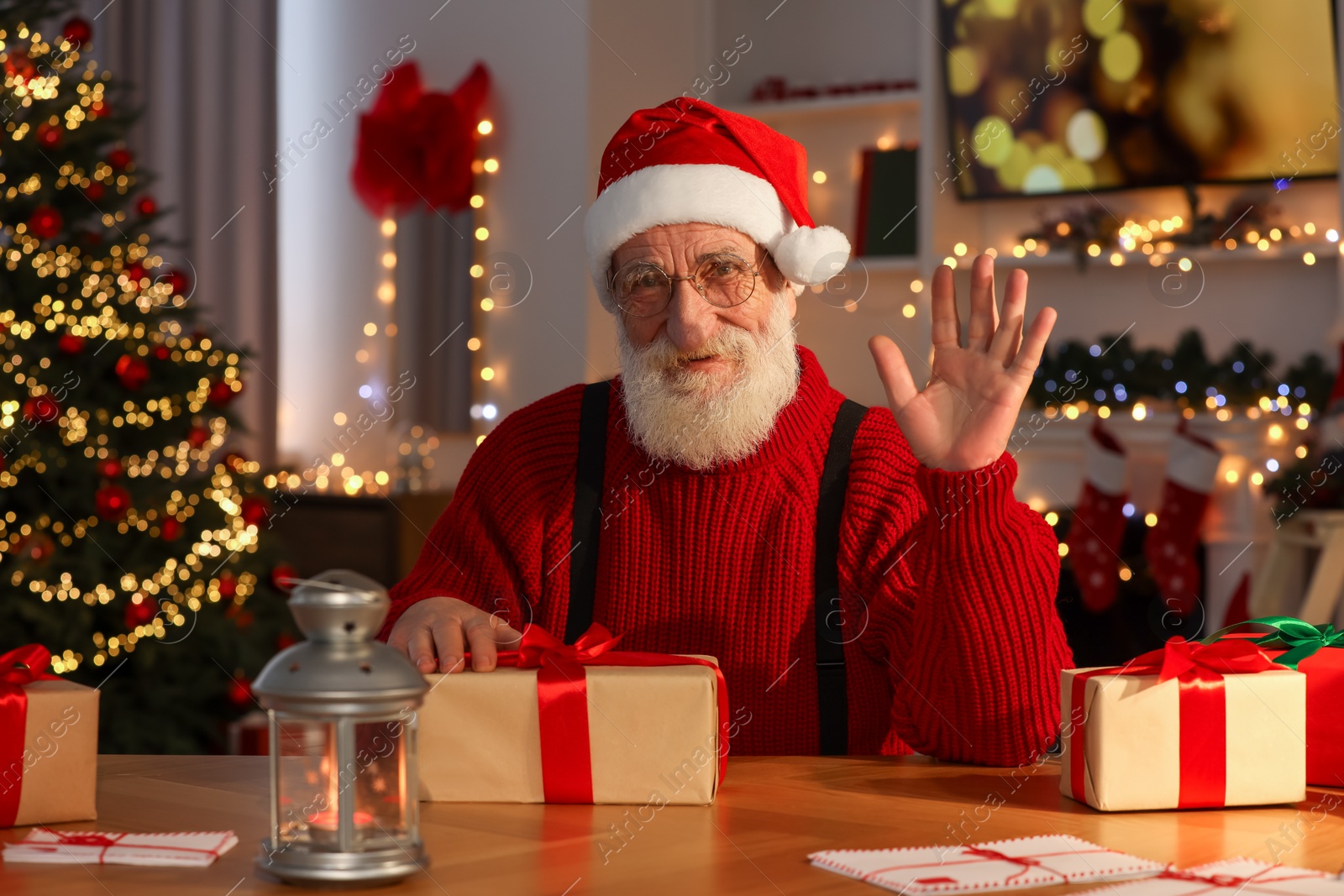 Photo of Santa Claus waving hello at his workplace in room decorated for Christmas