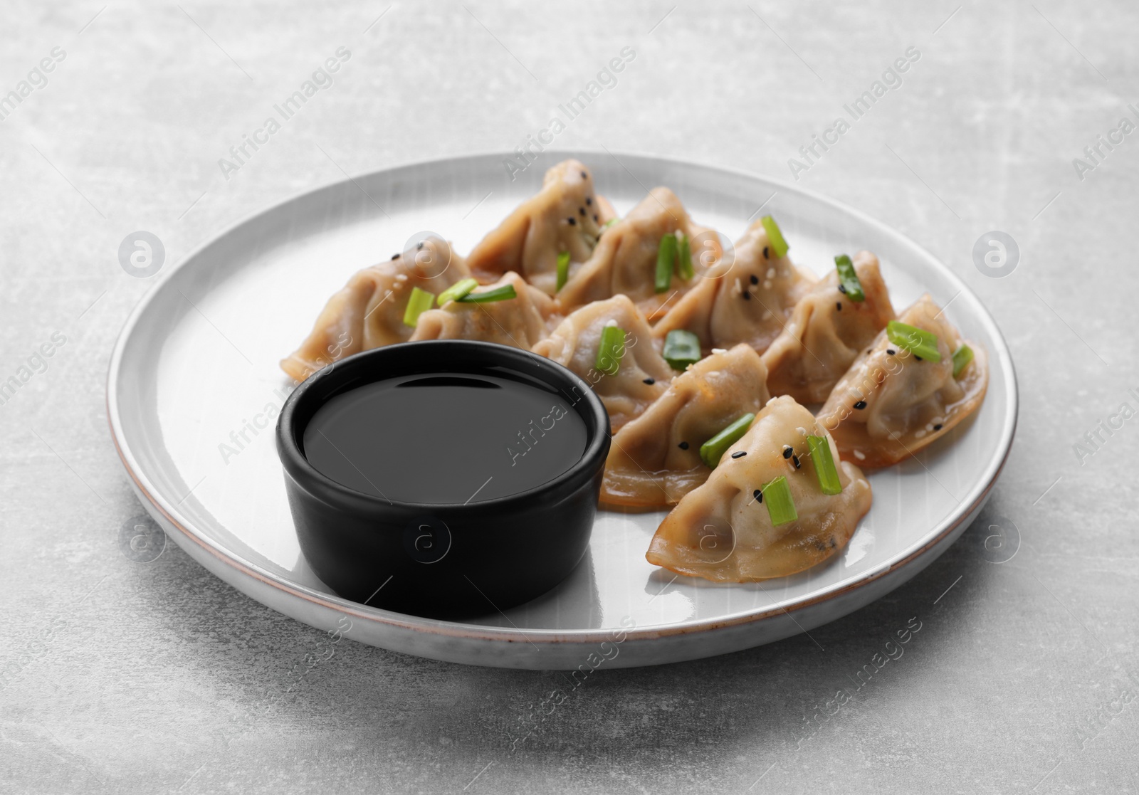 Photo of Delicious gyoza (asian dumplings) with green onions and soy sauce on light gray table, closeup