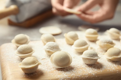 Photo of Wooden board with raw dumplings and blurred woman on background, closeup