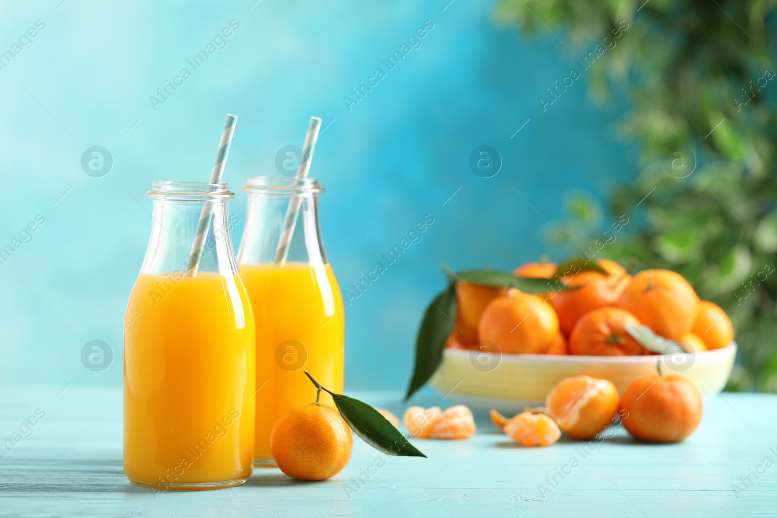 Photo of Bottles of fresh tangerine juice on blue wooden background. Space for text