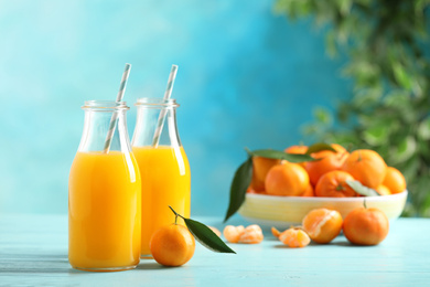 Photo of Bottles of fresh tangerine juice on blue wooden background. Space for text