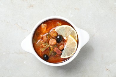 Meat solyanka soup with sausages, olives and vegetables in bowl on white textured table, top view