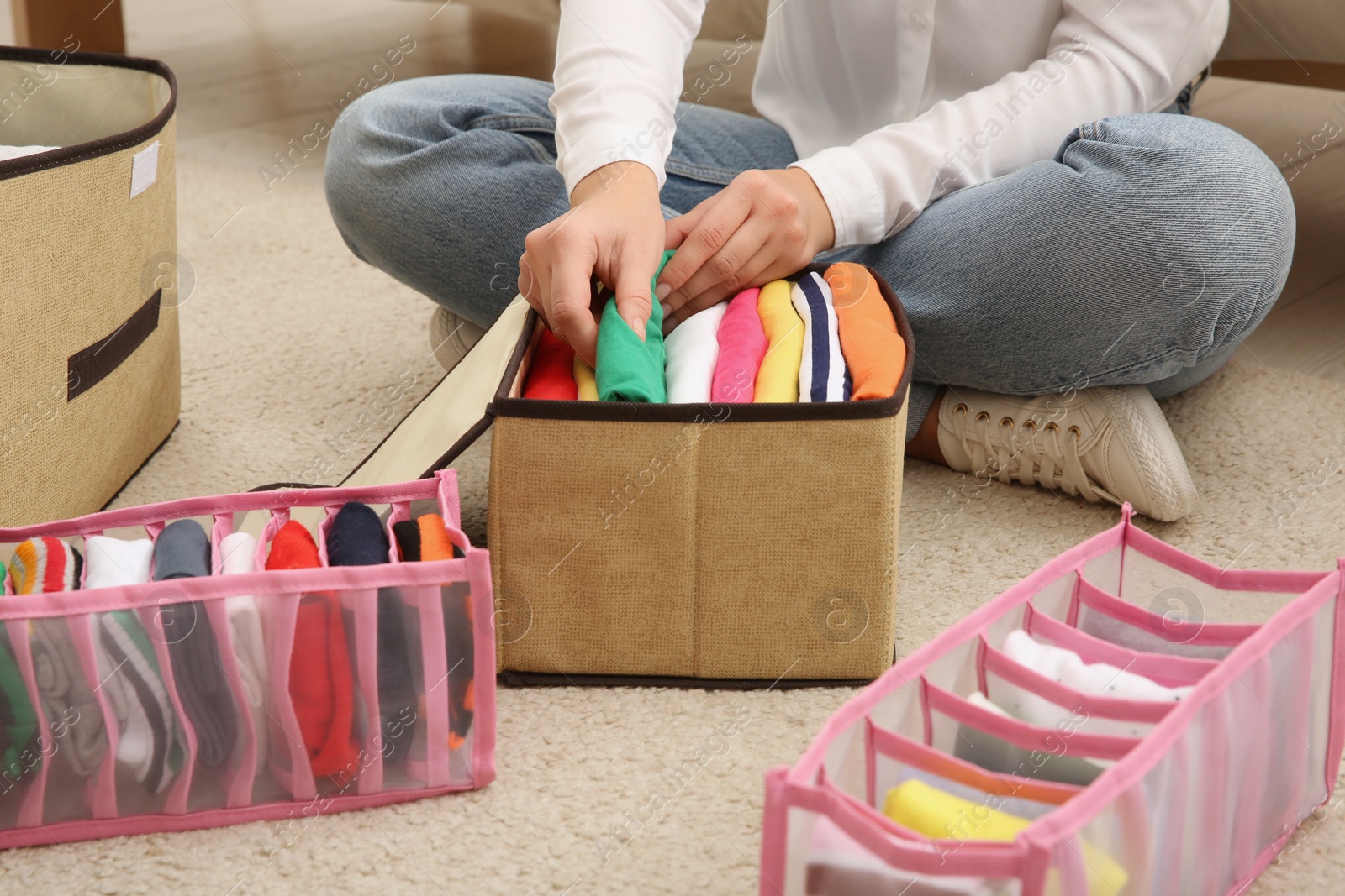 Photo of Woman folding clothes on floor at home, closeup. Japanese storage system