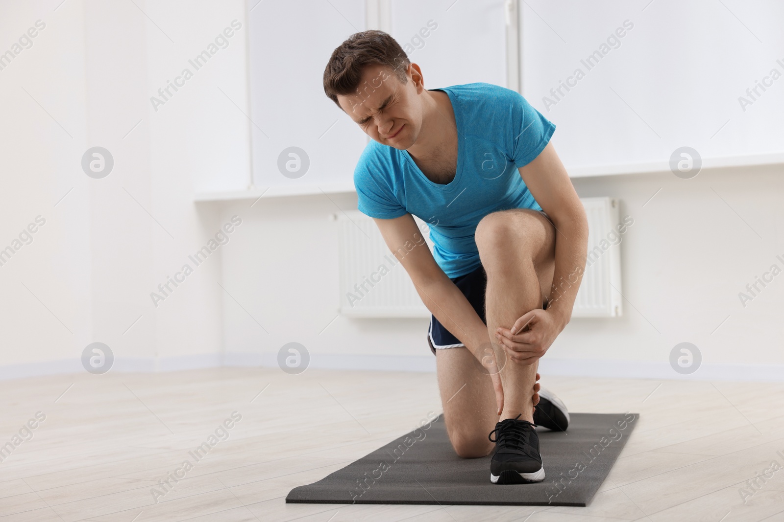 Photo of Man suffering from leg pain on mat indoors. Space for text