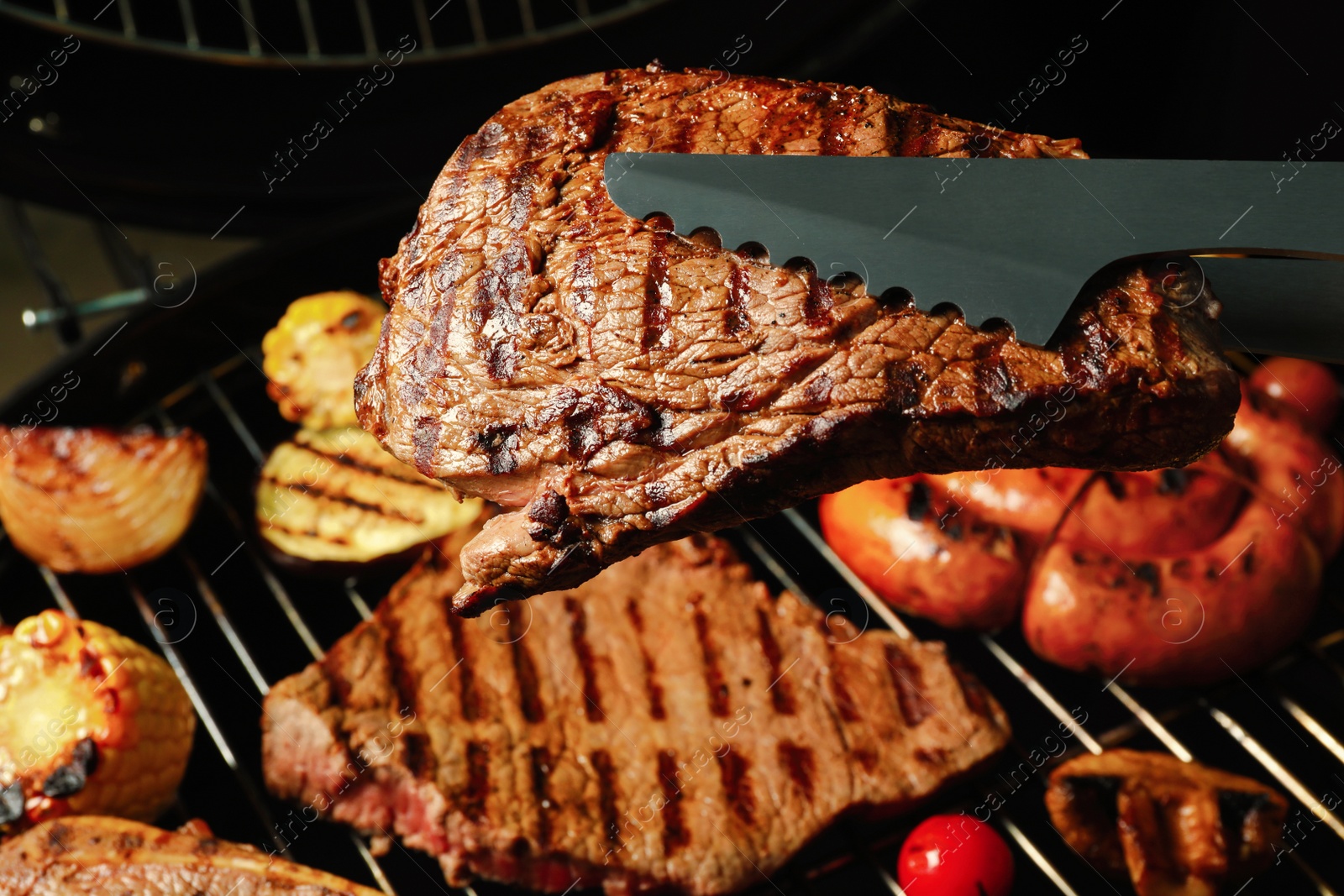 Photo of Tongs with fresh juicy meat steak over barbecue grill
