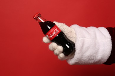 Photo of MYKOLAIV, UKRAINE - JANUARY 18, 2021: Santa Claus holding Coca-Cola bottle in hand on red background, closeup