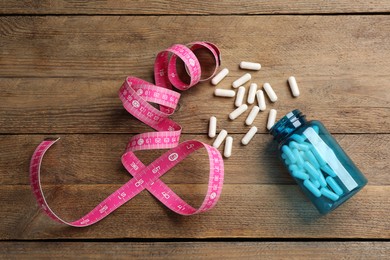 Photo of Jar of weight loss pills and measuring tape on wooden table, flat lay