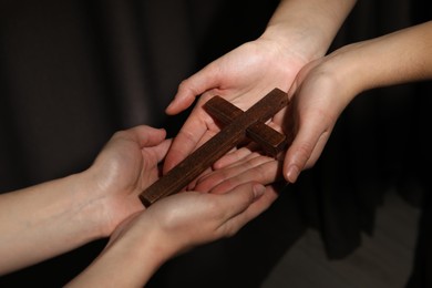 Easter - celebration of Jesus resurrection. Women holding wooden cross on dark background, closeup