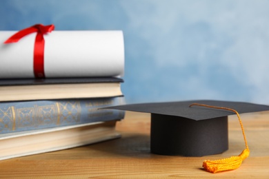 Graduation hat, books and student's diploma on wooden table against light blue background