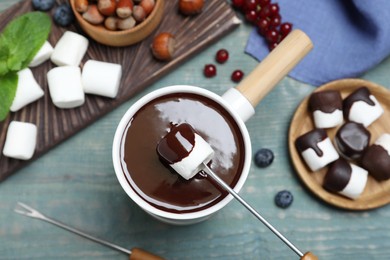 Photo of Dipping marshmallow into melted chocolate at blue wooden table, flat lay