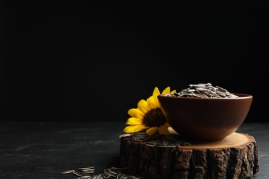Photo of Raw sunflower seeds and flower on black table against dark background. Space for text