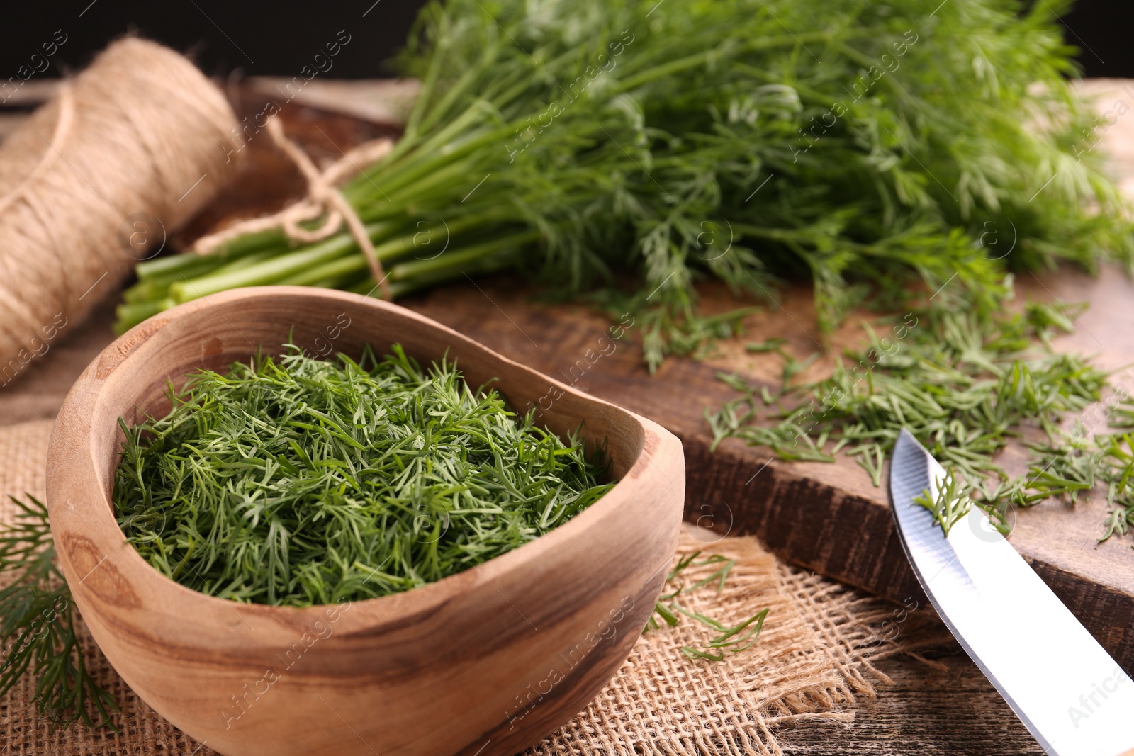 Photo of Fresh dill, cutting board and knife on wooden table, closeup