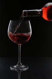 Photo of Pouring red wine from bottle into glass on black background