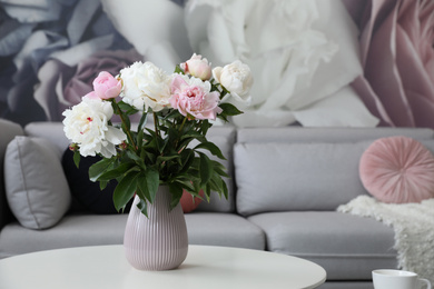 Photo of Bouquet of peonies on table near sofa in modern room. Interior design